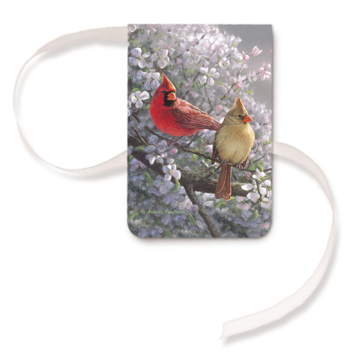 A magnetic bookmark with a ribbon, featuring an image of two cardinals perched on a branch with flowers in the background.
